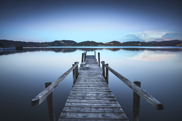 Wooden pier or jetty on blue lake sunset and sky reflection water. Long exposure Versilia Massaciuccoli Tuscany Italy.